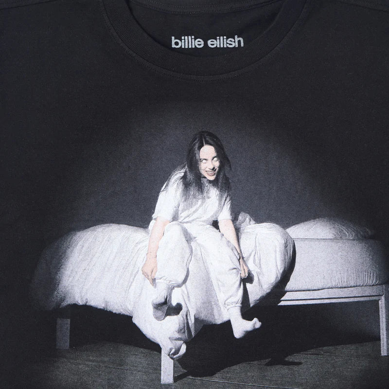 Close-up of the front print from the Billie Eilish anniversary tee, highlighting Billie’s ghostly expression and contrast-heavy image atop a white bed, set against a pitch-black background. Printed beneath the neckline with “billie eilish” logo.