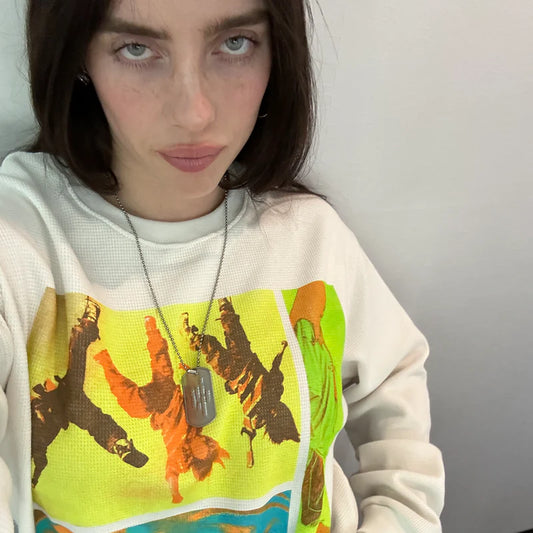 Close-up selfie of Billie Eilish wearing the “Birds of a Feather” collage thermal, highlighting the textured cream fabric and bold retro-style graphics. Bright, expressive colors give this thermal long sleeve a statement-making vibe.

