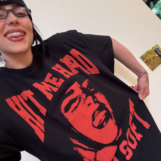 Billie Eilish wearing the “Hit Me Hard and Soft” T-shirt, sticking her tongue out playfully while showing off the bold red-on-black design featuring her own face and album title. Perfect fan-favorite Billie Eilish tour merch with edgy streetwear vibes.

