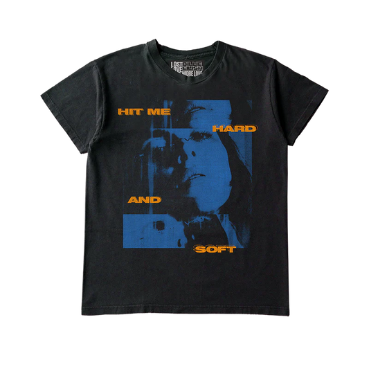 Black Billie Eilish x Lost Love T-shirt featuring a split-tone blue photo of Billie with bold orange “HIT ME HARD AND SOFT” text across the front. Official reworked merch tied to the “Hit Me Hard and Soft” album, printed on sustainable materials.

